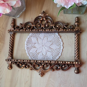 May include: A gold-toned decorative shelf with ornate scrollwork and a white crocheted doily on the top shelf.