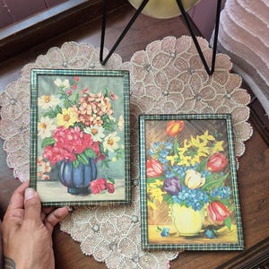 May include: Two rectangular framed prints featuring floral still life arrangements. The left print shows a blue vase with pink, yellow, and white flowers. The right print displays a yellow vase filled with red tulips, yellow daffodils, and blue flowers.