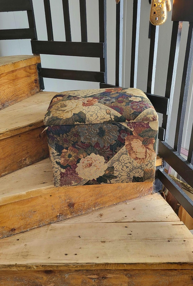 May include: A floral patterned storage ottoman with a square top. The ottoman is sitting on wooden stairs.