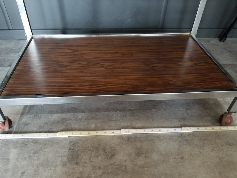 May include: A chrome metal serving cart with a wood-grain top. The cart has four wheels and a chrome metal frame.