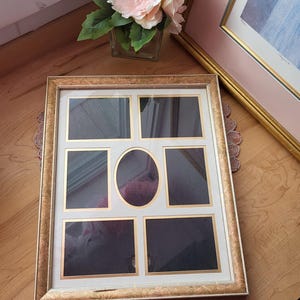 May include: A multi-photo frame with a gold-colored ornate border. The frame has six rectangular openings and one oval opening. A bouquet of pink and white flowers sits in a glass vase nearby.