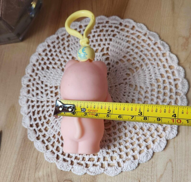 Puede incluir: Una alcanc&iacute;a de pl&aacute;stico rosa con un clip amarillo y un dije de luna azul. La alcanc&iacute;a mide aproximadamente 10 cm de alto.