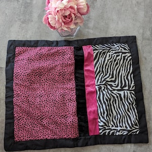Puede incluir: Una almohada de tiro con estampado rosa y negro con un borde negro. La almohada está hecha de una tela suave y mullida y presenta un estampado de cebra en un lado y un estampado de leopardo rosa en el otro.