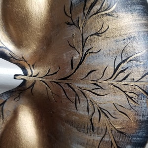 May include: A decorative wooden tray with a gold and black painted design of a tree branch. The tray has a unique shape and is perfect for serving snacks or drinks.