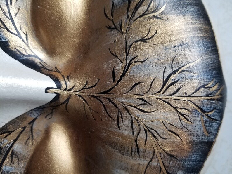 May include: A decorative wooden tray with a gold and black painted design of a tree branch. The tray has a unique shape and is perfect for serving snacks or drinks.