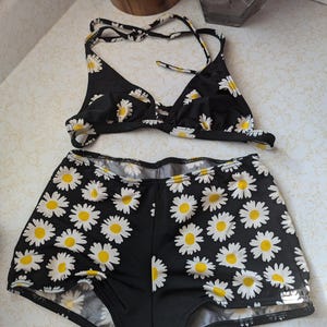 May include: Black bikini with a white daisy print. The top is a halter style and the bottoms are high waisted.