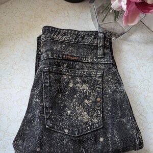 May include: Black acid wash jeans with a brown "Guess" logo on the back pocket.