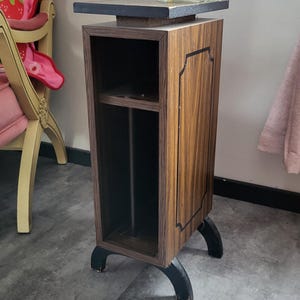 Può includere: Un tavolino in legno in stile vintage con finitura scura, pannello decorativo e ripiano. Il tavolo ha gambe nere curve e un piano scuro. Un vaso di vetro con fiori rosa è posto sopra. Altezza: circa 76 cm.
