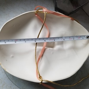 May include: White masquerade mask with a gold and pink ribbon attached. The mask is 9 inches wide.