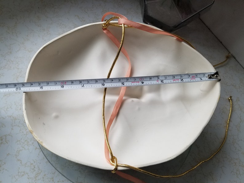May include: White masquerade mask with a gold and pink ribbon attached. The mask is 9 inches wide.