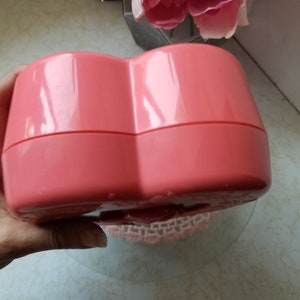 May include: A heart-shaped pink plastic box with a hinged lid. The box is closed and appears to be empty.