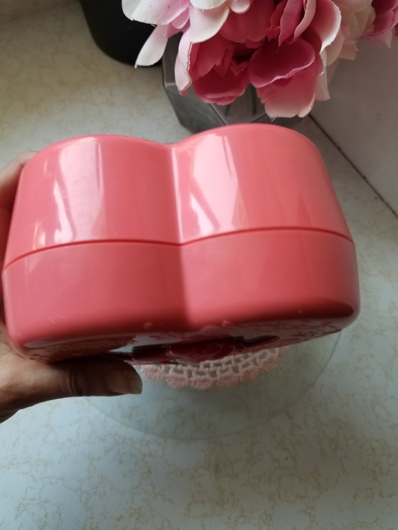 May include: A heart-shaped pink plastic box with a hinged lid. The box is closed and appears to be empty.