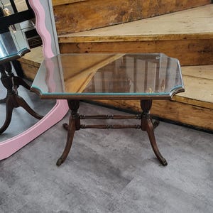 Op de afbeelding: Een bijzettafel met een glazen blad en een houten frame. De tafel heeft een rechthoekig glazen blad en een eenvoudig ontwerp.