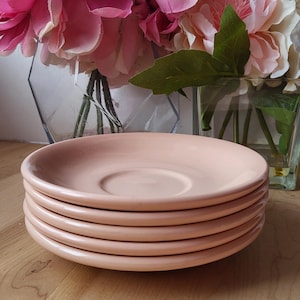 May include: A stack of four pale pink saucer plates. The plates are smooth and glossy.