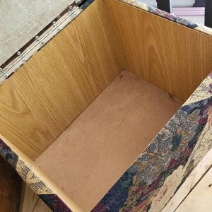 May include: An open storage ottoman with a wooden frame and a floral patterned fabric exterior. The inside of the ottoman is lined with a brown material.
