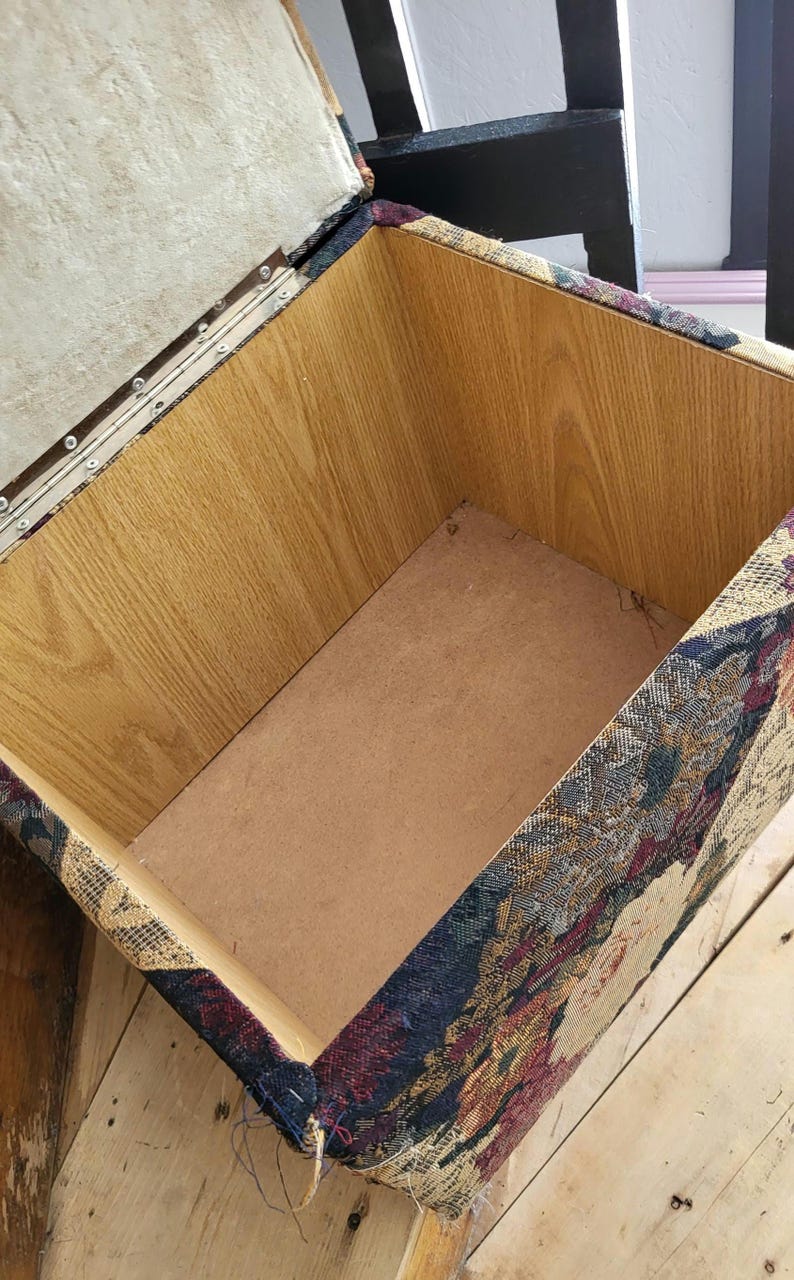 May include: An open storage ottoman with a wooden frame and a floral patterned fabric exterior. The inside of the ottoman is lined with a brown material.