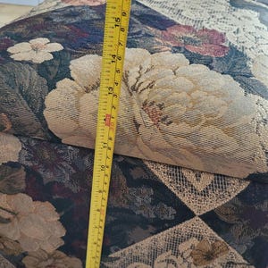 May include: A floral patterned fabric storage box with a yellow measuring tape next to it. The tape measures 17 inches.