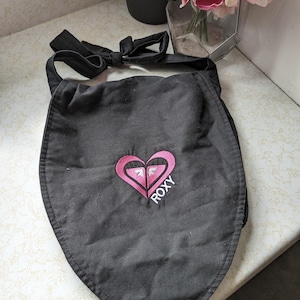 May include: Black triangular apron with a pink heart logo that says "ROXY" in white lettering.