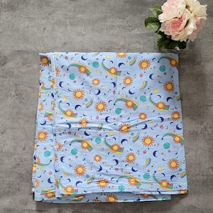 May include: A blue fabric with a repeating pattern of suns, moons, stars, and planets. The suns are yellow with orange rays, the moons are blue, the stars are white, and the planets are green and blue.