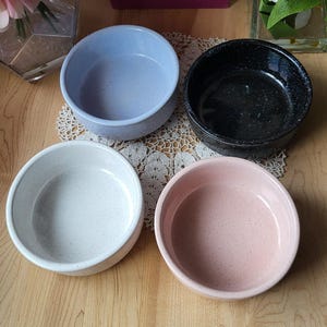 Puede incluir: Cuatro cuencos de cerámica en diferentes colores y patrones. Los cuencos son azul claro con motas blancas, negro con motas blancas, blanco con motas grises y rosa con motas blancas.