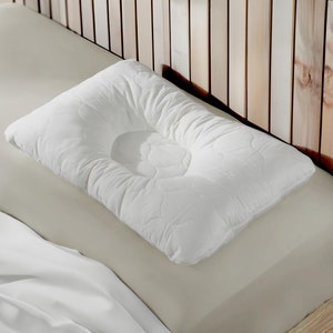 May include: A white contoured pillow with a quilted surface, resting on a beige bed.
