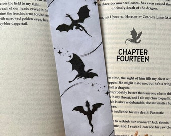 May include: A white bookmark with black silhouettes of dragons and stars. The bookmark has the text "CHAPTER FOURTEEN" printed on it.
