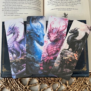 Op de afbeelding: Set van vier draken-bladwijzerontwerpen. De bladwijzers tonen een paarse, blauwe, roze en zwarte draak op een bloemige achtergrond. De tekst op de bladwijzer luidt "Major Andora's Guide to the Riders Quadrant (Unauthorized Edition)"