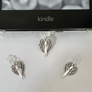 May include: Three silver bookmark charms with a heart-shaped design featuring a dagger with wings. The charms are attached to clear plastic holders.
