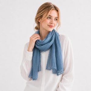 Könnte beinhalten: Ein hellblauer Schal mit zarter Spitzenborte. Der Schal ist um Hals und Schultern drapiert. Der Stoff wirkt leicht und weich. Der Hintergrund ist schlicht weiß. Ein stilvolles Accessoire.