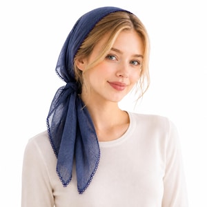 Op de afbeelding: Een marineblauwe hoofddoek met een geschulpte rand is aan de achterkant van het hoofd geknoopt. De hoofdbedekking is gemaakt van een transparante stof. De persoon op de foto draagt een wit shirt met lange mouwen.