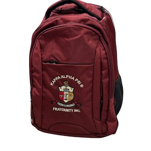 May include: Maroon backpack with the Kappa Alpha Psi Fraternity Inc. emblem embroidered on the front. The backpack has a top handle, a front pocket, and a black mesh side pocket. The emblem features a crest with the fraternity's name.