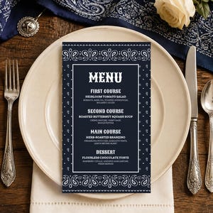 May include: A rectangular menu card with a dark blue and white paisley border. The text reads: MENU, FIRST COURSE HEIRLOOM TOMATO SALAD, SECOND COURSE ROASTED BUTTERNUT SQUASH SOUP, MAIN COURSE HERB-ROASTED BRANZINO, DESSERT FLOURLESS CHOCOLATE TORTE.