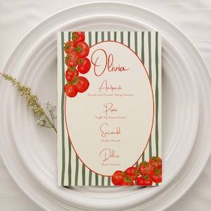 Op de afbeelding: Een menukaart met de naam "Olivia" in cursief schrift, met een rode ovale rand en een groen gestreepte achtergrond. Het menu bevat "Antipasto", "Primo", "Secondo" en "Dolce" met beschrijvingen van gerechten. Trossen rode kerstomaten sieren de boven- en onderkant.