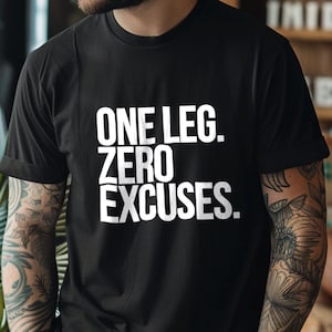 Puede incluir: Camiseta negra con el texto blanco "ONE LEG. ZERO EXCUSES." La camiseta de manga corta parece estar hecha de un material suave. La persona que lleva la camiseta tiene tatuajes en los brazos.