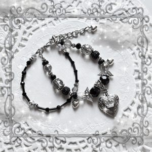 May include: Two beaded bracelets. One is black with clear beads, the other is black and clear with silver accents. One bracelet has a heart-shaped pendant with a crown and angel wings.