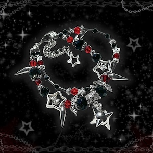 May include: A gothic-style necklace with a black background and star accents. The necklace features silver-toned metal, black and red beads, and star-shaped pendants. The design includes spikes and a chain border.