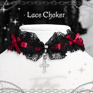 May include: A black lace choker with red ribbon detailing and a silver cross pendant. The text "Lace Choker" is displayed above the choker. The choker is displayed on a white mannequin.