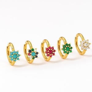 Op de afbeelding: Vijf goudkleurige oorringen, elk versierd met een bloemvormige cluster van edelstenen. De edelstenen zijn turquoise, veelkleurig, rood, groen en helder. De oorbellen worden getoond tegen een witte achtergrond.