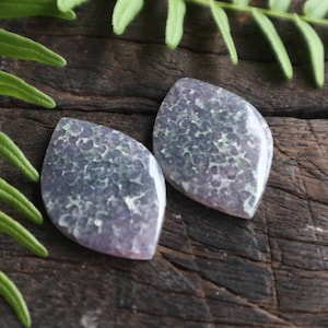May include: Two purple and green agate cabochons with a unique, speckled pattern. The cabochons are shaped like teardrops and have a smooth, polished surface.