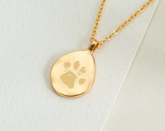 May include: A gold chain necklace with a teardrop-shaped pendant featuring a paw print design.