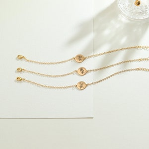 May include: Three gold-colored chain bracelets with oval pendants, each featuring a different floral design. The bracelets have a delicate chain and a lobster clasp closure. The pendants have engraved floral illustrations.