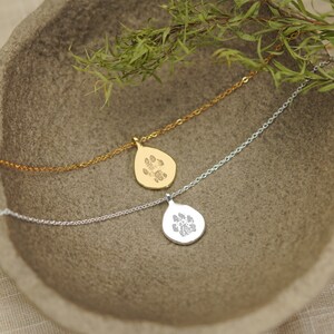 Puede incluir: Dos collares con colgantes en forma de l&aacute;grima, uno en oro y otro en plata. Cada colgante presenta un dise&ntilde;o grabado de una huella de animal. Los colgantes est&aacute;n unidos a finas cadenas de metal a juego, con un dise&ntilde;o sencillo y limpio.