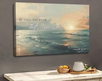 May include: Canvas art print featuring an ocean scene with a sunset. The artwork displays the text "BE STILL AND KNOW That I am God" in elegant script. The bottom right corner includes "PSALM 46:10". The color palette includes blues, oranges, and whites.