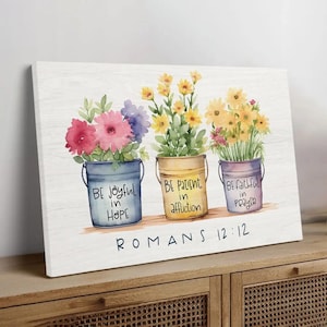 May include: Watercolor painting on canvas featuring three buckets of flowers. Each bucket is a different color: blue, yellow, and purple. Text on the buckets reads "Be joyful in Hope", "Be patient in affliction", and "Be faithful in prayer". The text "Romans 12:12" is below.