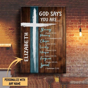 May include: Wooden wall art with a cross design. The artwork features the words "God Says You Are..." followed by inspirational words like "Strong" and "Precious." A name can be personalized on the left side.