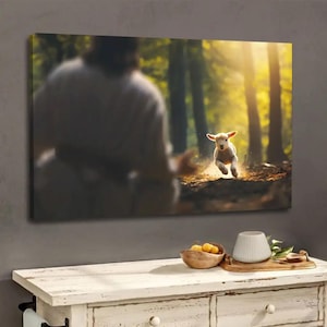 May include: A canvas print depicts a lamb running through a sunlit forest. The lamb is the focal point, with a blurred figure in the background. The artwork is displayed above a white wooden cabinet with decorative items.