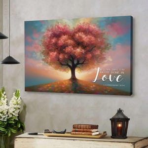 May include: A canvas print featuring a tree with a heart-shaped canopy in shades of pink and red. The artwork includes the text "LET ALL THAT YOU DO BE DONE IN Love" and "1 CORINTHIANS 16:14" against a sunset backdrop.