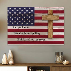 May include: Wooden wall art featuring the American flag with a wooden cross overlay. The flag design includes red and white stripes and a blue field with white stars. The text reads, "In this house, We stand for the flag, And kneel for the cross."