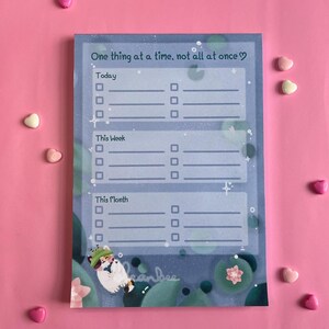 May include: A blue and green illustrated notepad with a cat illustration and the text "One thing at a time, not all at once♡". The notepad has sections for "Today", "This Week", and "This Month" with checkboxes for each section.