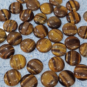May include: A collection of round, polished tiger's eye stones. The stones are a mix of brown, gold, and black colors with a shimmering, iridescent effect.
